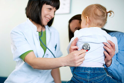A mother holding a child whilst a GP examines them