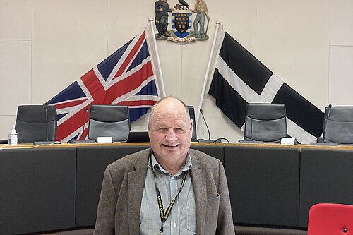Councillor Jim Candy stands in front of the British and Cornish flags in a council chamber