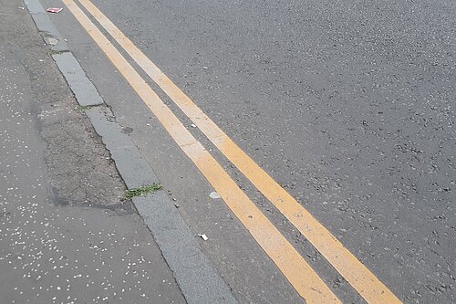 A set of double yellow lines running alongside a kerb on a grey road.