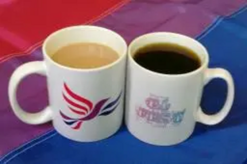 A Bisexual Liberal Democrats mug, and a Brighton BiFest mug, on a Bi Flag, containing tea and coffee
