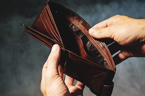 A person opening a wallet to reveal it is empty.