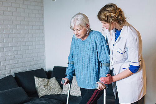 Carer helping older person on crutches