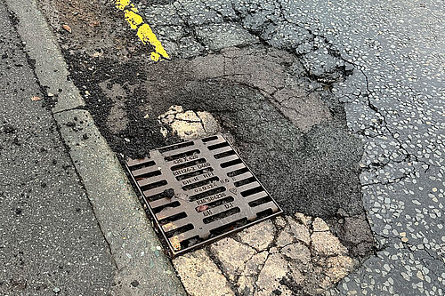A grid with significant damage to the road surface surrounding it 