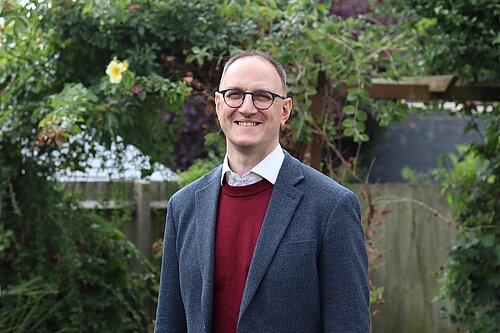A headshot of Ian Sollom with nature in the background