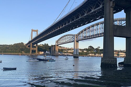 The bridge across the River Tamar at the Saltash Crossing, taken from underneath the bridge on the Cornish side. It is a clear day and boats are visible on the water.