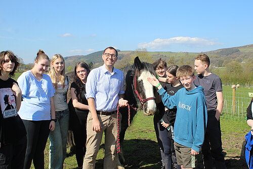 Tom Gordon MP stands in field with horse and group of young carers 
