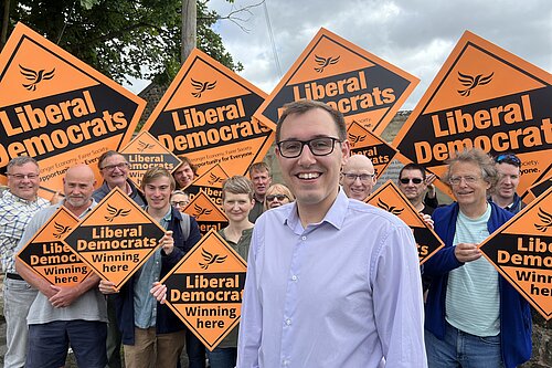 Tom Gordon stood in front of supporters holding Diamond shaped placards with Liberal Democrats written on them