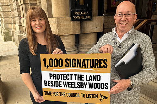 Cllr Nicola Aisthorpe and Liberal Democrat campaigner Brian Barrett holding a sign outside Grimsby Town Hall celebrating 1,000 petition signatures to protect land beside Weelsby Woods.