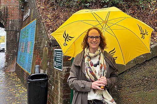 Alison holding a yellow umbrella outside Wivelsfield Station