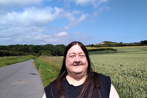 Margaret Crosby on Foxcover Lane standing in front of farmland and the Hastings hill